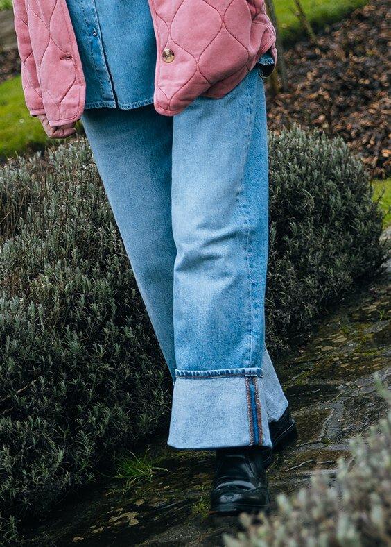 a person in a pink jacket and jeans standing in a garden
